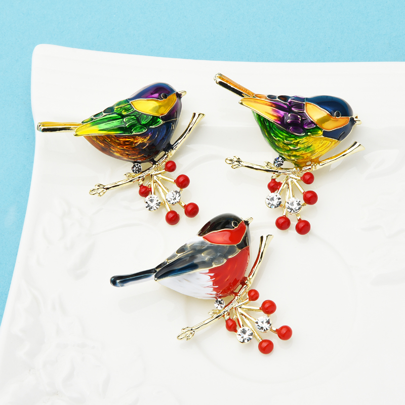 Broche Rouge Gorge en métal émaillé avec détails rouges et noirs, posée sur une branche décorative avec baies rouges