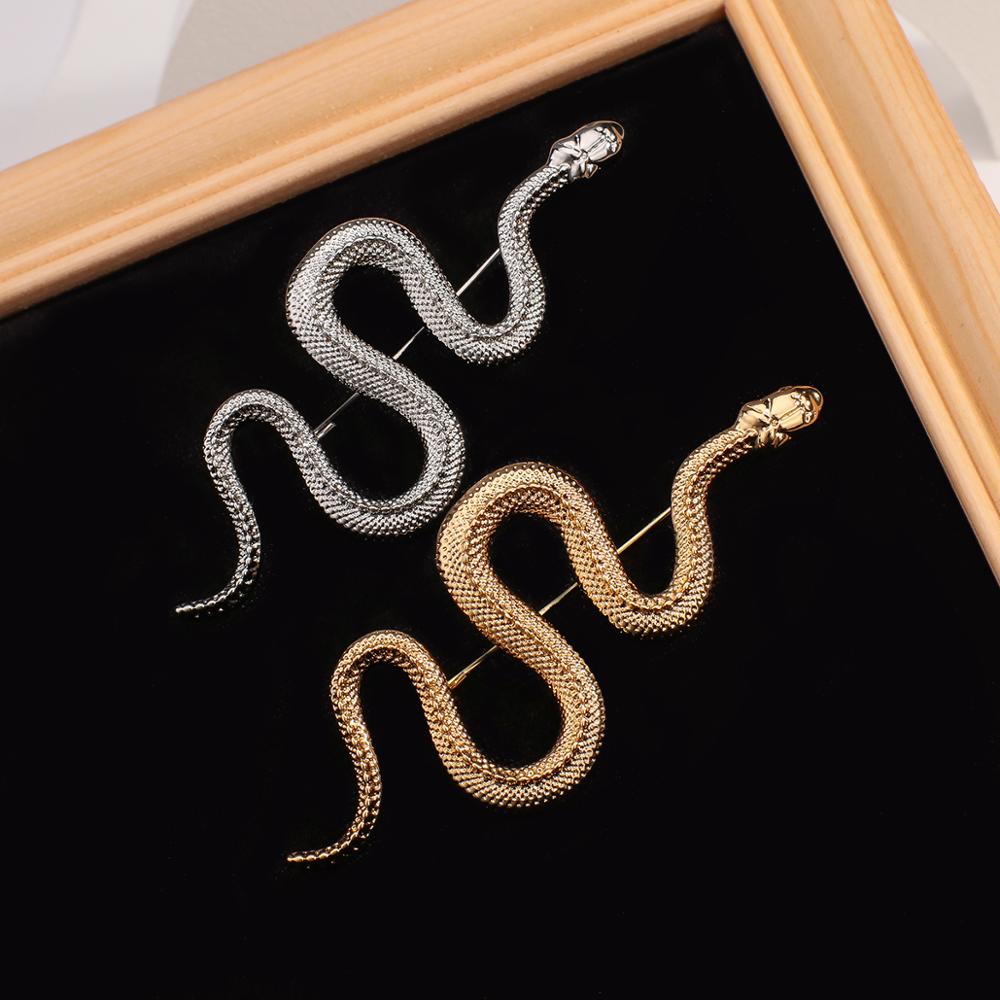 Broche serpent en métal doré et argenté avec finition texturée posée sur fond noir dans un cadre en bois clair
