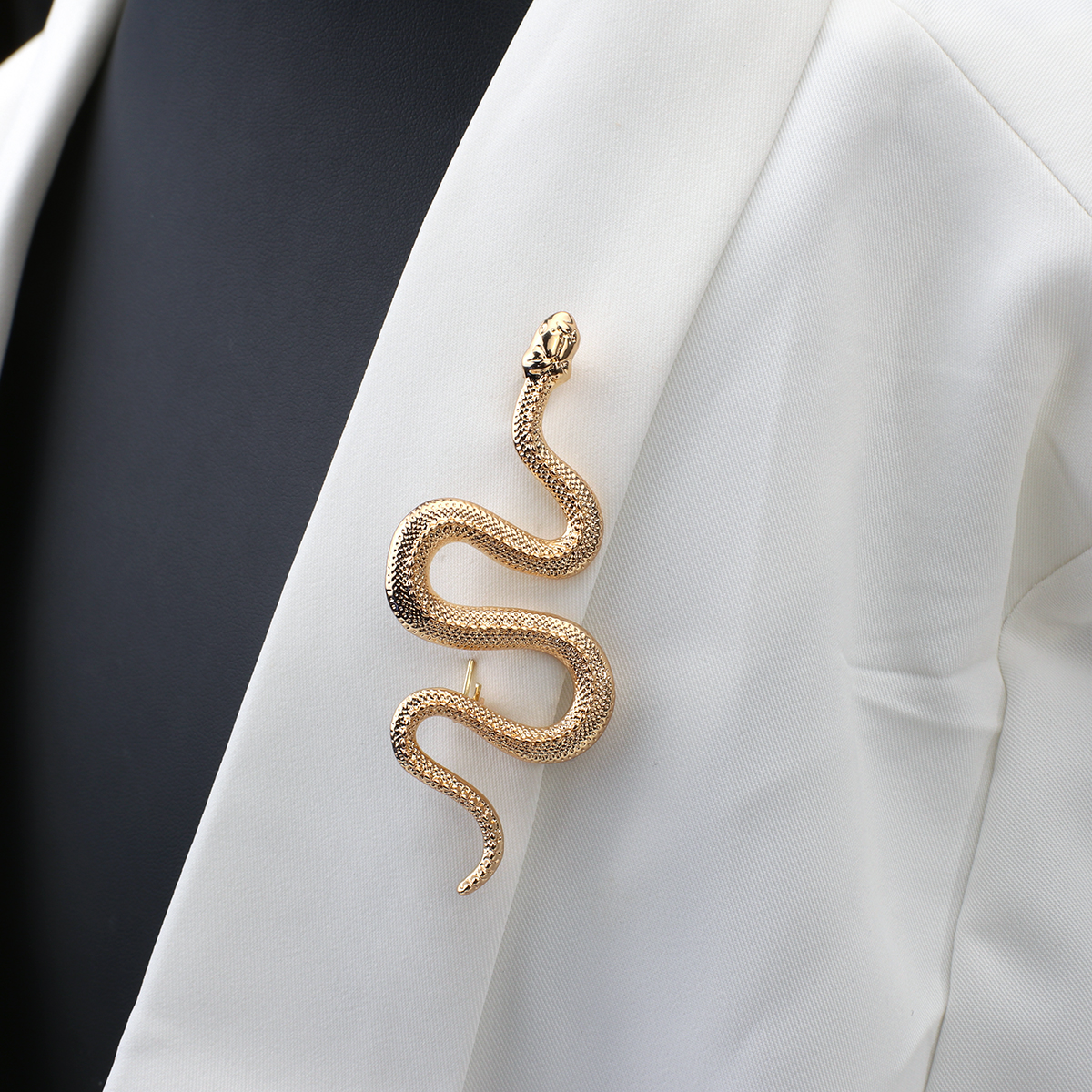 Broche serpent dorée en métal avec finition texturée portée sur un blazer blanc vue de côté