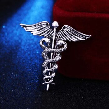 Broche argentée représentant un serpent enroulé autour d'un bâton ailé, détail soigné des ailes et des écailles du serpent