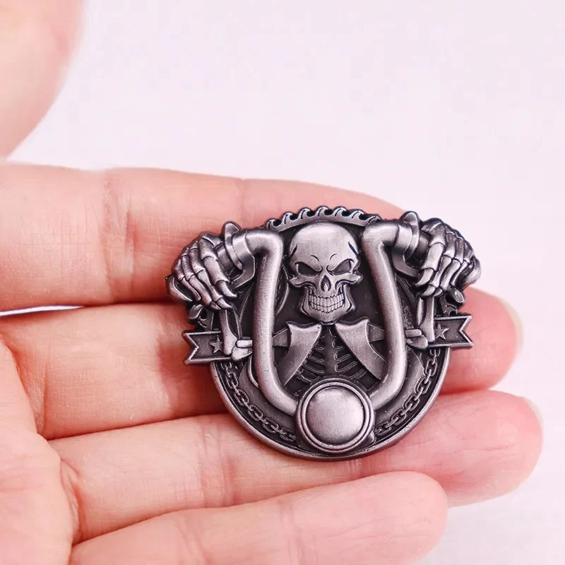 Broche Skull Biker en métal argenté avec motif tête de mort et mains tenant un anneau, détail du design travaillé