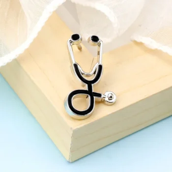 Broche stéthoscope médecin en métal argenté avec détails noirs posée sur un coin de bois clair