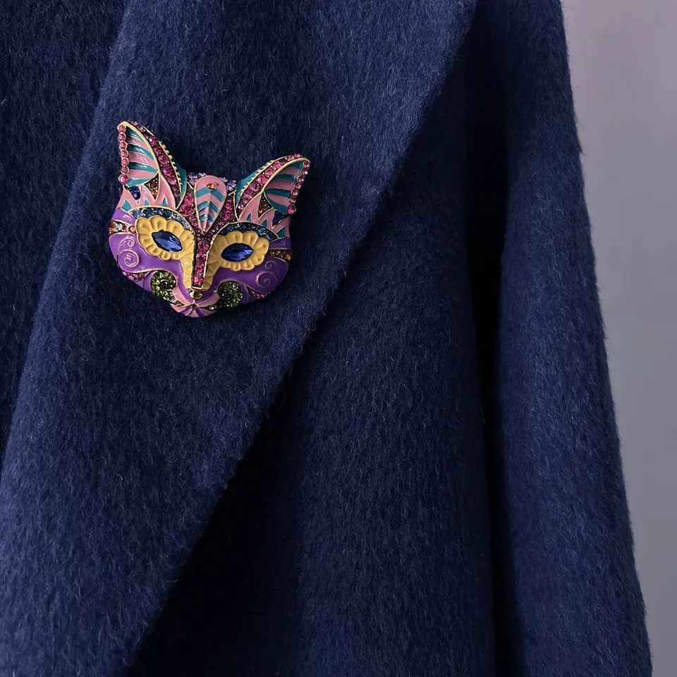 Broche tête de chat noir et blanc en émail coloré avec motifs décoratifs portée sur un manteau bleu marine