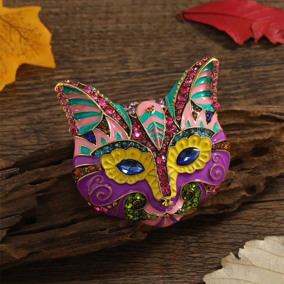 Broche tête de chat noir et blanc colorée avec motifs roses, verts et violets, ornée de strass et détails dorés, vue en gros plan sur fond bois