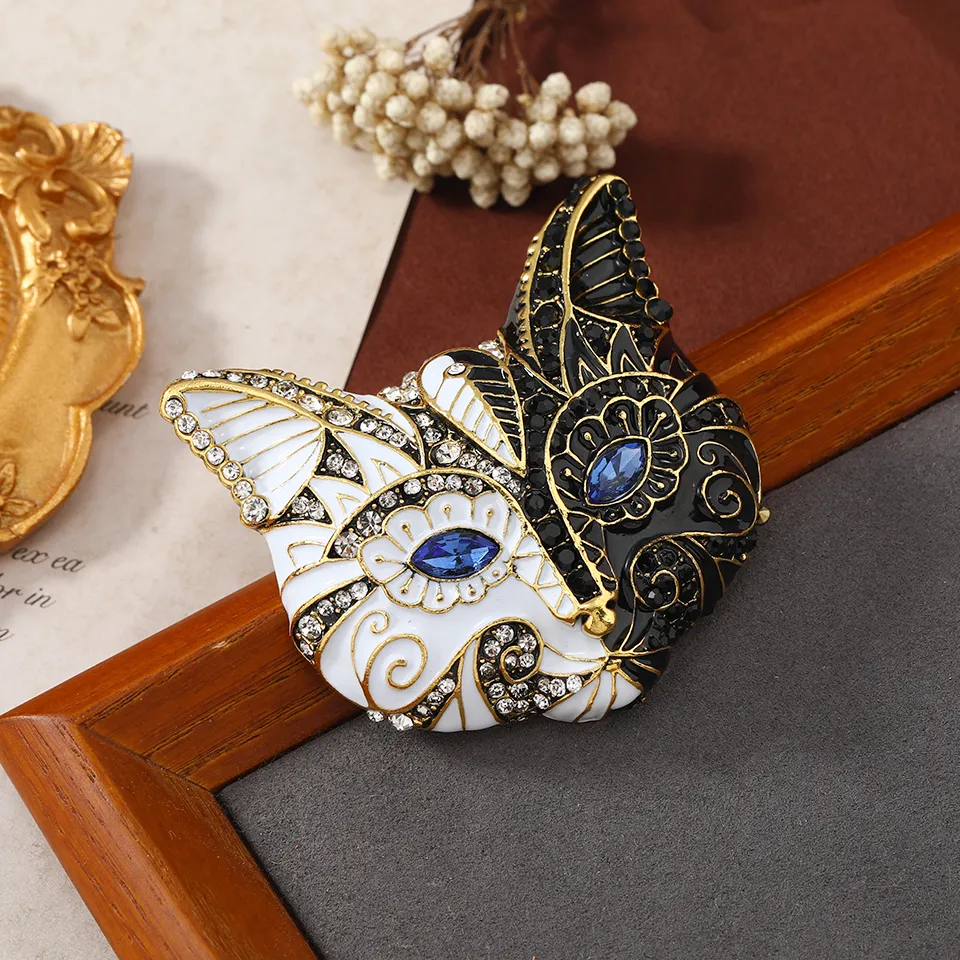 Broche tête de chat noir et blanc en métal avec détails dorés et pierres bleues, vue en gros plan sur un cadre en bois