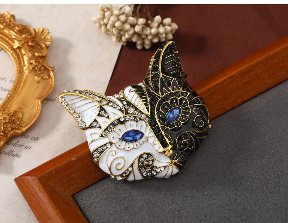 Broche tête de chat noir et blanc en métal émaillé avec détails dorés et yeux bleus, motif décoratif élégant