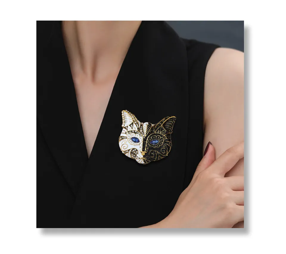 Broche tête de chat noir et blanc en métal doré avec détails bleus portée sur un vêtement noir