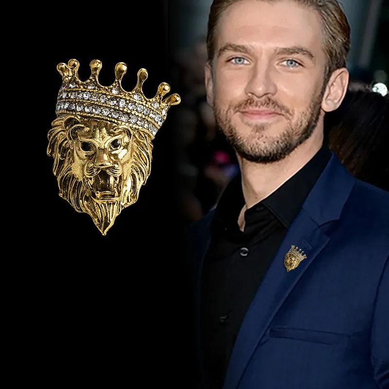 Broche tête de lion dorée avec couronne ornée de strass portée sur revers de veste bleu marine