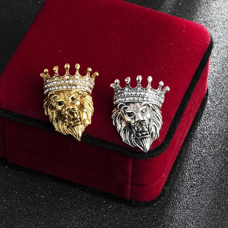 Broches tête de lion en métal doré et argenté avec couronne et détails soignés posées sur un écrin rouge