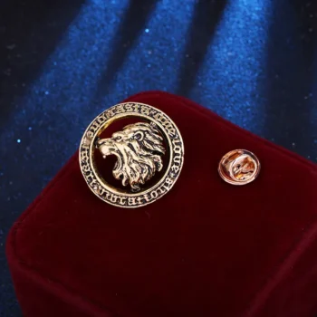 Broche tête de lion dorée en métal avec motif sculpté, présentée sur un coussin rouge