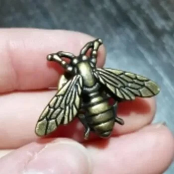 Petite broche abeille en métal bronze avec ailes détaillées tenue entre deux doigts