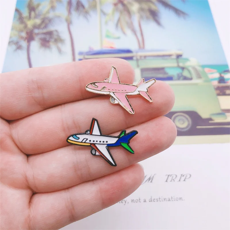 Pin's avion en émail avec un modèle rose et un modèle blanc bleu vert, détail soigné des couleurs et contours métalliques