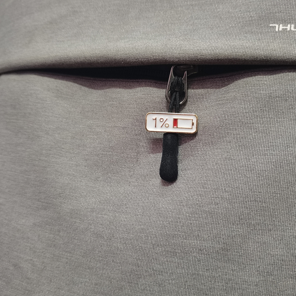 Pin's barre d'énergie en métal avec motif batterie à 1% et finition émaillée blanche et rouge accroché sur tissu gris