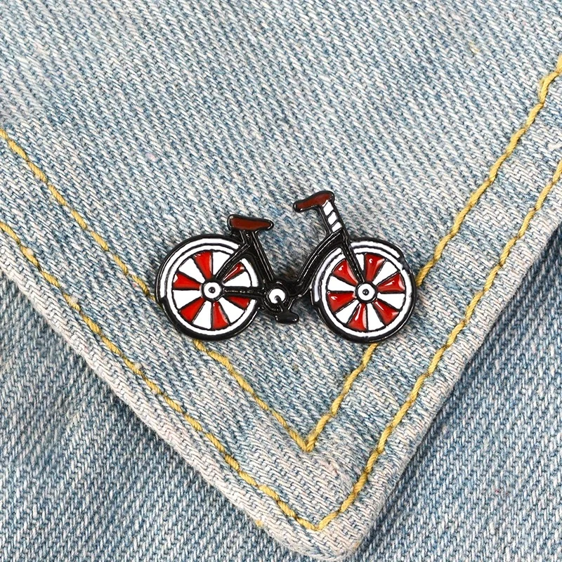 Pin's bicyclette noir avec roues rouges et blanches fixé sur un tissu jean bleu clair avec couture jaune