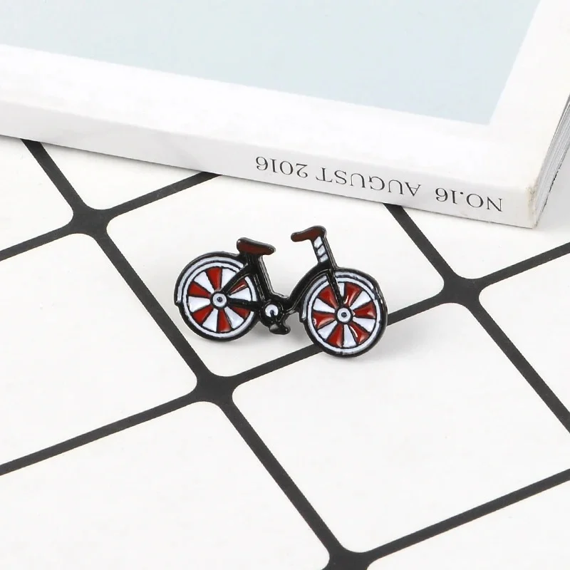 Pin's bicyclette noir avec roues rouges et blanches en métal émaillé, posé sur un carrelage blanc et noir
