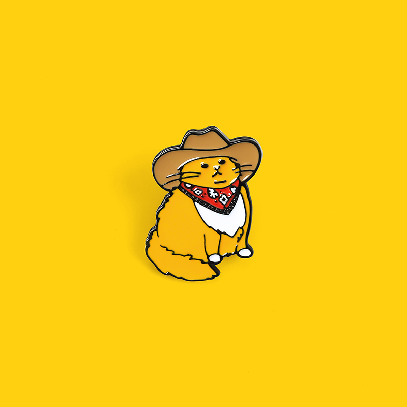 Pin's chat orange portant un chapeau de cowboy marron et un bandana rouge à motifs blancs