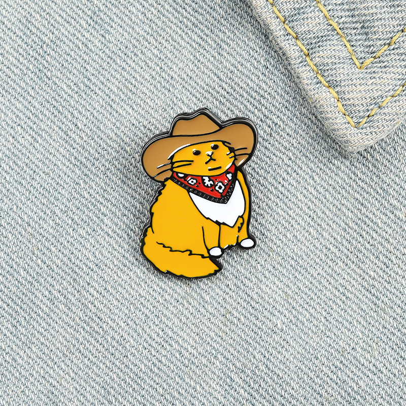 Pin's Chat Cowboy en métal émaillé, chat orange avec chapeau marron et bandana rouge, posé sur tissu jean clair