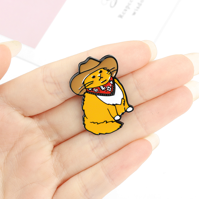 Pin's Chat Cowboy en métal émaillé jaune avec chapeau marron et bandana rouge, détail soigné visible en gros plan dans une main