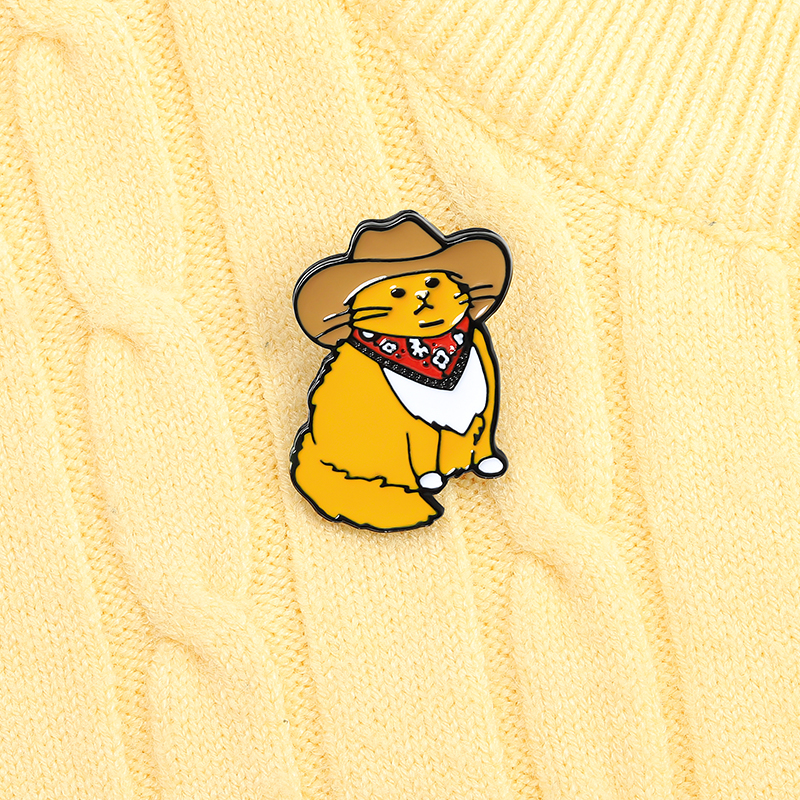 Pin's chat orange en tenue de cowboy avec chapeau marron et bandana rouge sur pull jaune