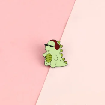 Pin's dinosaure vert clair avec lunettes de soleil noires et casque audio rouge sur fond bicolore rose clair et beige
