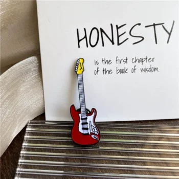 Pin's guitare électrique rouge avec manche jaune et détails blancs et noirs posé sur surface rayée devant carte avec texte