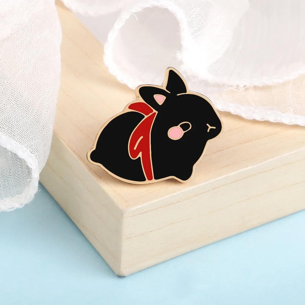 Pin's lapin mignon noir avec nœud rouge en émail, détail soigné sur fond clair