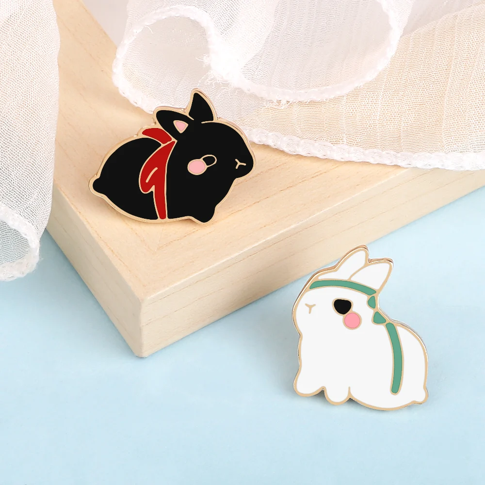 Pin's lapin mignon noir avec nœud rouge en émail, détail soigné sur fond bois clair et tissu blanc