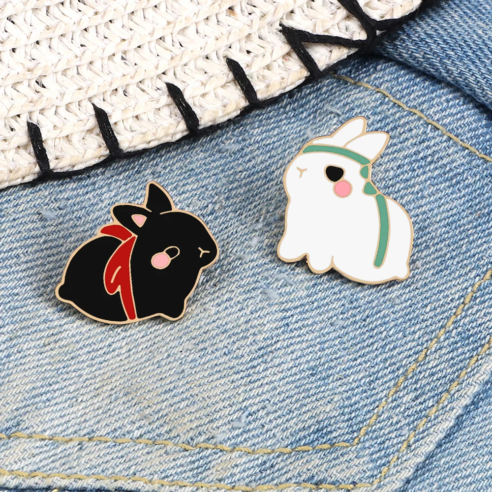 Pin's Lapin Mignon noir avec foulard rouge et pin's Lapin Mignon blanc avec rayures vertes posés sur jean bleu