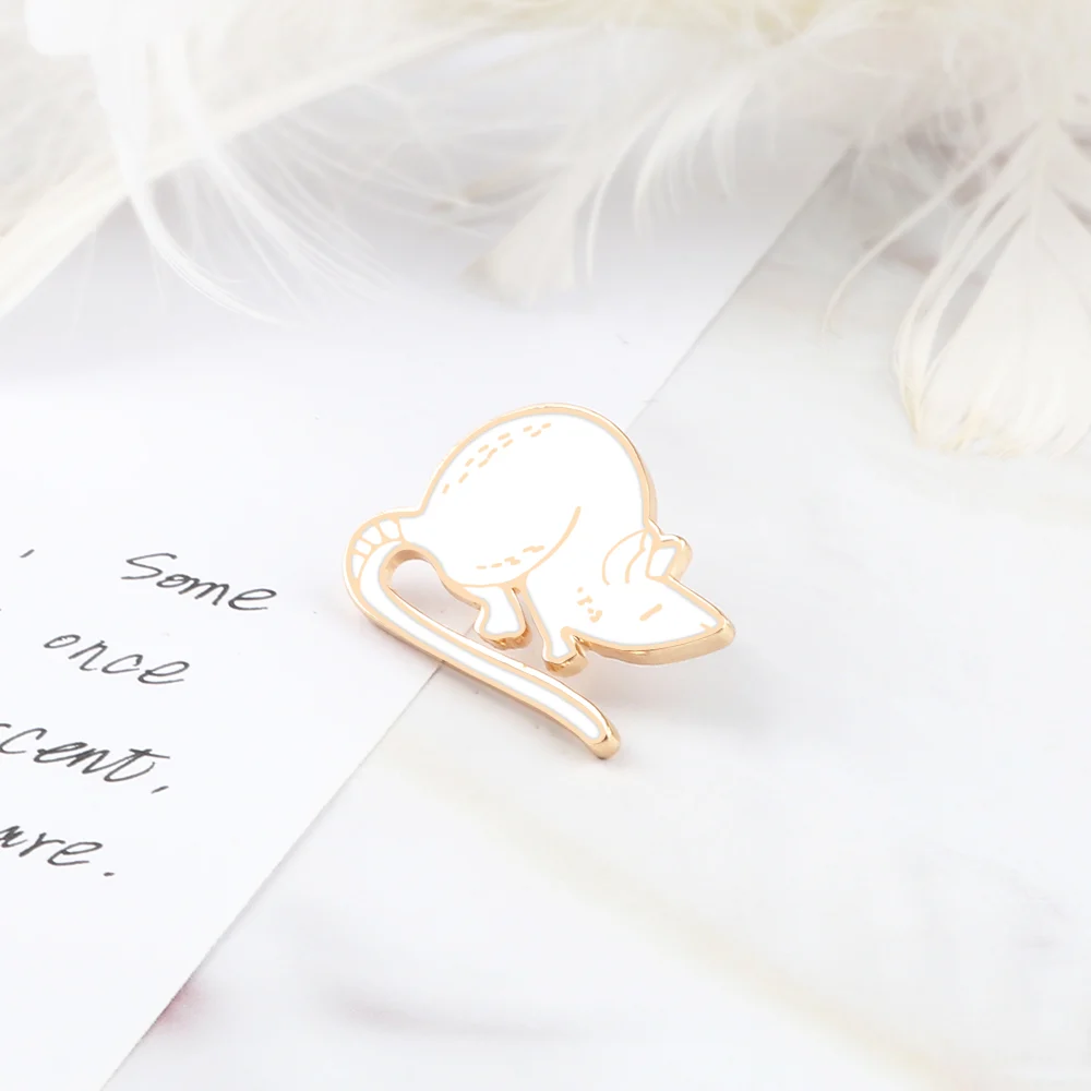 Pin's Souris en métal blanc avec contour doré posé sur surface claire avec plume en arrière-plan