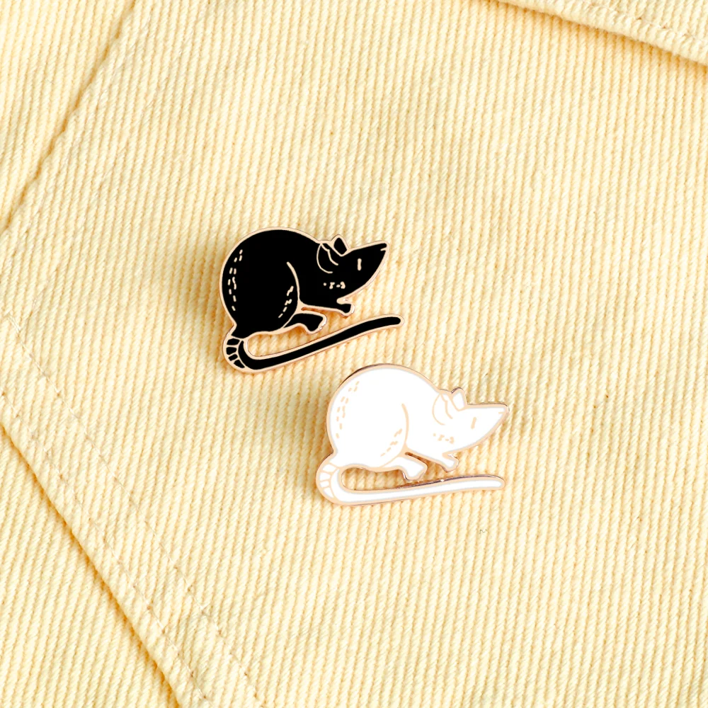 Pin's Souris noir et blanc en émail avec finition soignée posés sur tissu beige à rayures fines