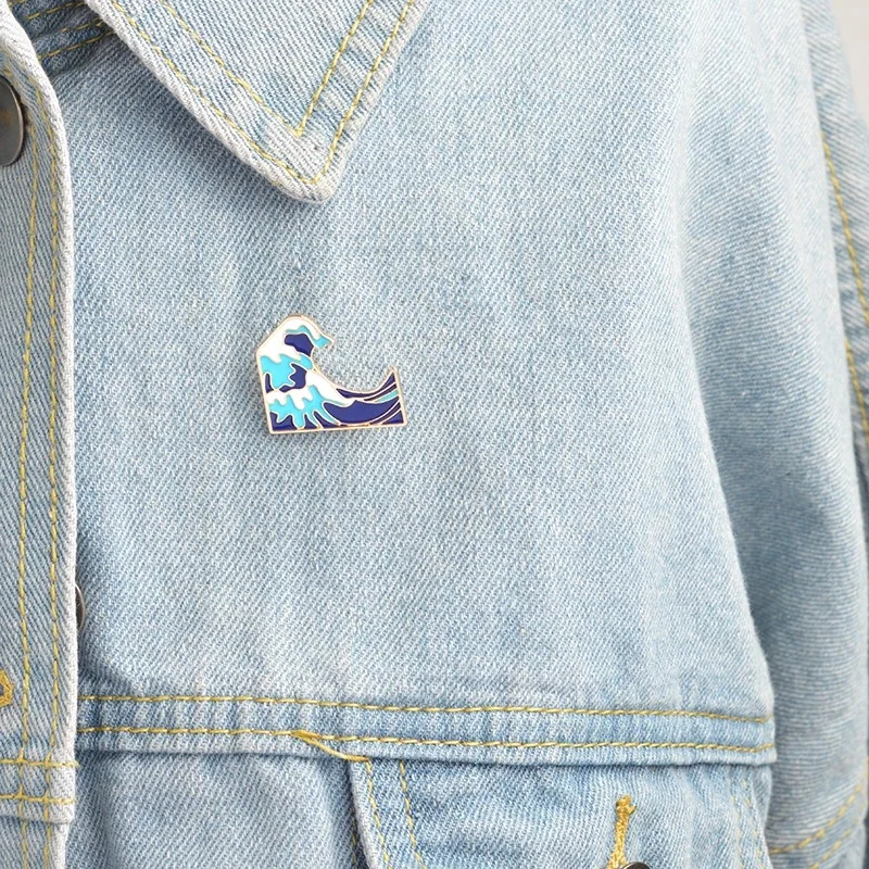 Pin's Vague en métal émaillé bleu et blanc fixé sur une veste en jean clair, détail du pin's en gros plan