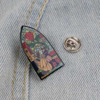 Pin's vitrail en forme de vitrail coloré avec motif floral rouge, bleu et jaune sur fond noir, posé sur tissu jean clair