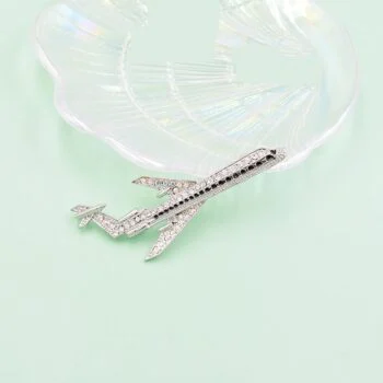 Broche avion en métal argenté ornée de strass multicolores posée sur une coupelle en verre transparent