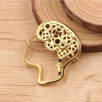 Broche cerveau dorée en métal avec engrenages ajourés et strass noirs, silhouette de profil, détail soigné
