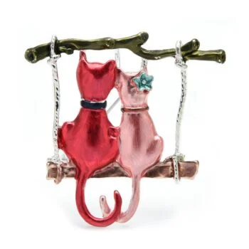 Broche couple de chat rouge et rose en métal émaillé assis sur une balançoire en métal vert et marron avec détail fleur bleue