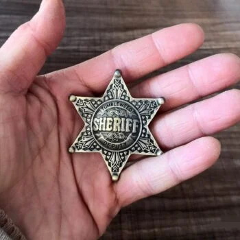 Broche étoile de shérif en métal bronze avec gravures décoratives tenue dans une main