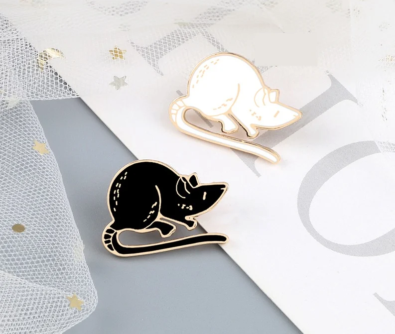Pin's Souris en métal émaillé noir et blanc avec contour doré, vue rapprochée sur deux modèles contrastés posés sur un fond clair avec tulle et étoiles dorées