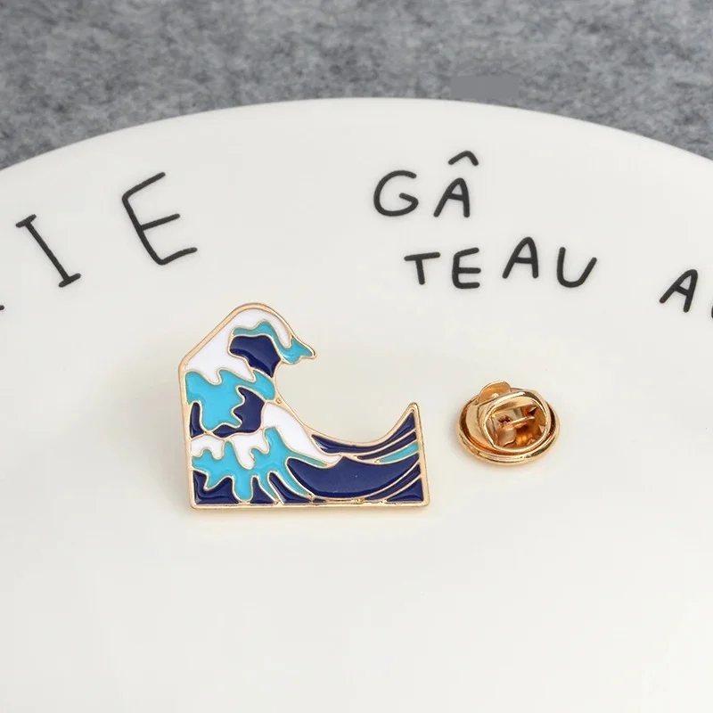Pin's vague en métal doré avec émail bleu clair et bleu foncé, détail de la forme stylisée d'une vague
