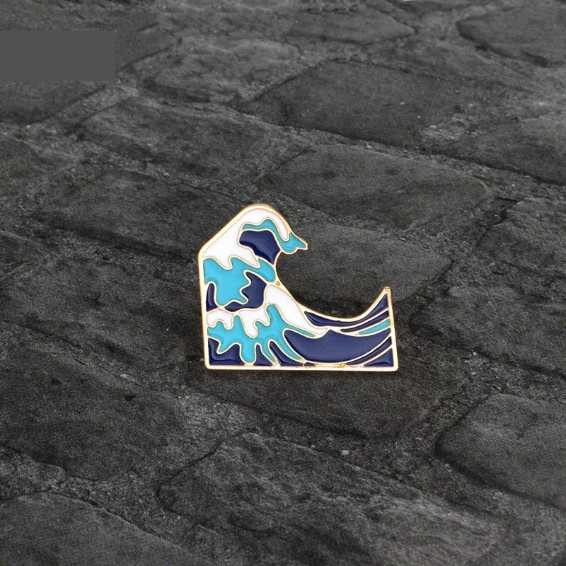 Pin's Vague en métal avec émail bleu, turquoise et blanc, motif vague stylisée avec contour doré, détail soigné